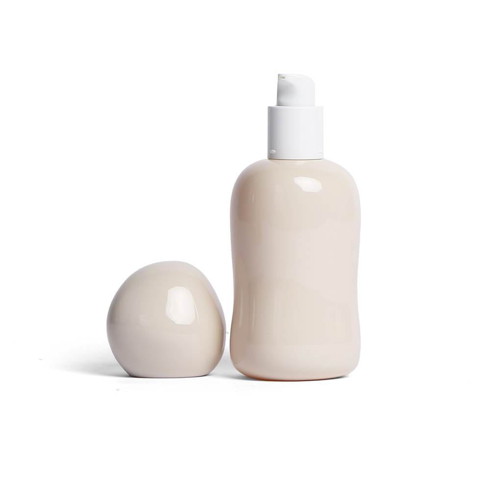 Minimalist cream-colored Opal lubricant glass bottle with rounded sculptural design and pump top, with the lid sitting beside.